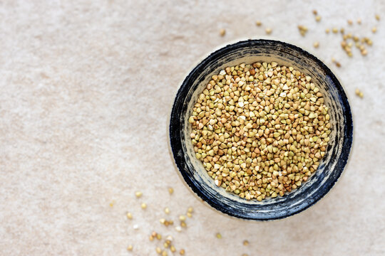 Hulled buckwheat grains in a rustic bowl against light stone background