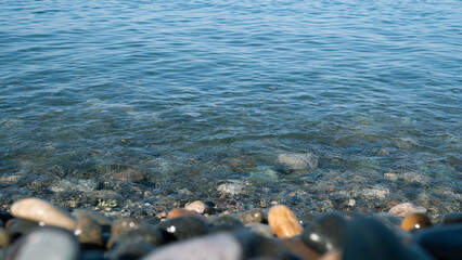 Clear blue water gently washing over smooth, colorful pebbles on a tranquil shoreline