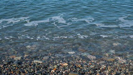 Clear blue water gently washing over smooth, colorful pebbles on a tranquil shoreline
