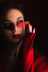 Young Woman In Red Suit With Red Lips And Sunglasses Posing On The Black Background