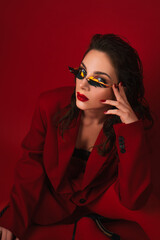 Young Woman In Red Suit With Red Lips And Sunglasses Posing On The Red Background