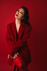Young Woman In Red Suit With Red Lips And Sunglasses Posing On The Red Background