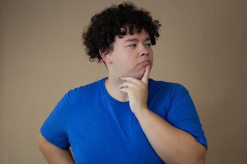 Thoughtful man wearing a blue shirt, touching his chin with a curious and focused look. Perfect for...