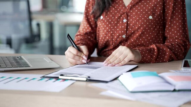 Close up of a female hand signing documents at a desk at a workplace in a modern business office. Young businesswoman boss looks through the folder with documentation and signs the contract with a pen