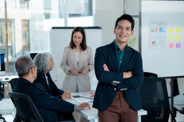 Portrait of a smiling asian businessman standing with crossed arms in a meeting room during a...