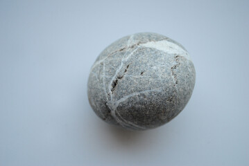 Round gray stone with natural white veins and cracks on a neutral background. Aesthetic and textured surface, highlighting geological patterns and organic beauty.