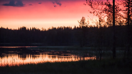 Reflection of sunset colours on the surface of a lake in the forests of eastern Finland on a summer night