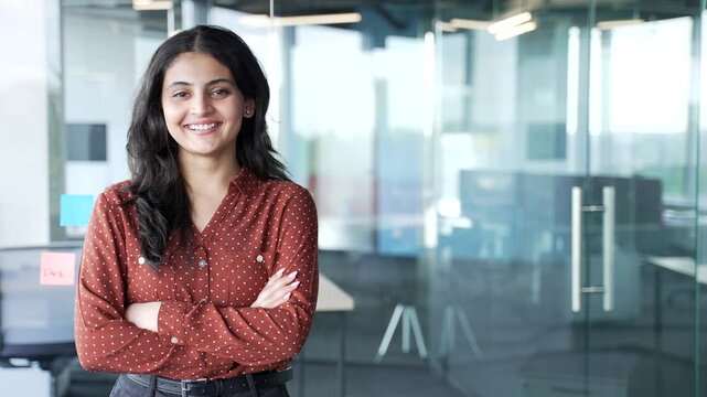 Portrait of young smiling businesswoman standing at workplace in modern business office. Happy confident female employee looking at camera. Empty copy space for writing text. Template for advertising