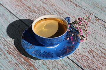 An old blue porcelain cup with coffee and some flowers on the table. Blue porcelain cup with coffee. 