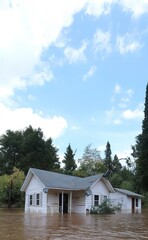 A house is partially submerged in floodwaters, with water lapping at its base and extending into the foreground. Flooded houses under water, the flood. Environmental disaster
