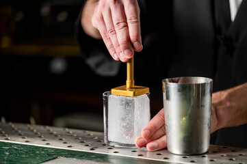 A bartender using an ice press on a large ice block to create a perfectly shaped ice for cocktails at a bar.
