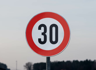 A speed limit sign displaying the number 30, within a red circle, against a pale, overcast sky.