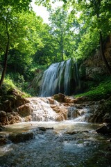 Obraz premium Waterfall in forest flows over rocks. Green trees surround the water. Cool water cascade landscape. Natural scenery with flowing stream. Scenic view outdoor.
