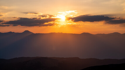 The setting sun over the mountains, the beautiful sun's rays shine through the clouds, the natural background, freedom, tranquility and peace