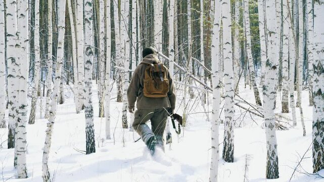 A lone hunter with a gun is walking through a winter forest.  Tracks down wild forest animals and hunts them. Hunting animals is a way of life.
