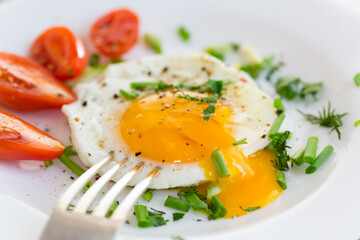 Fried eggs with greens and tomatoes on a white plate