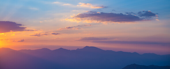 Beautiful clouds at sunset over mountains, rays of sunshine, beautiful light, natural background, calm and tranquility