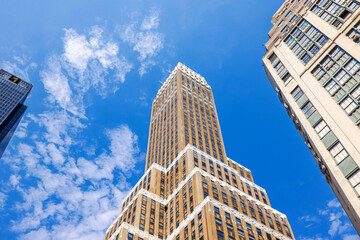 Historic skyscraper with brown brick facade against blue sky with white clouds in New York. USA.