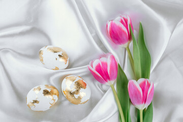 Gold white Easter eggs with pink tulips, top view,  on a white silky backdrop, Easter festive banner.