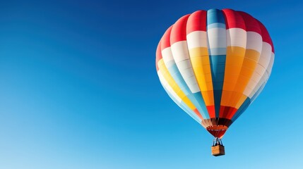 Obraz premium A stunning hot air balloon with a mix of vibrant colors rises against a deep blue sky, symbolizing excitement and the joy of adventure among the clouds.