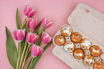 Easter gold eggs in a carton box with tulips  on a pastel pink background.