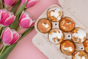 Easter gold eggs in a carton box with tulips  on a pastel pink background.