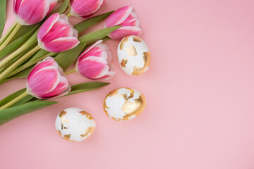 Easter gold eggs with tulips on a pastel pink background.
