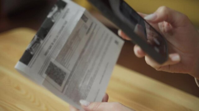 A woman holds her smartphone over a letter, scanning the QR code. The background features soft lighting and a comfortable atmosphere, enhancing her focus on the task.