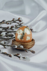 Golden Easter egg in a nest with willow branches  close up on a white silky backgorund, Easter banner.