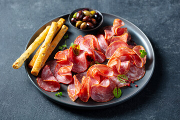 Cured meat, sausage assortment platter, charcuterie with olives and grissini bread sticks. Close up.