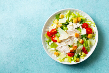 Caesar salad with chicken in a white plate. Blue background. Copy space. Top view.