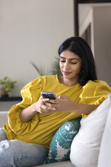 Pretty Indian woman spend pastime at home using modern smartphone, chatting through mobile...