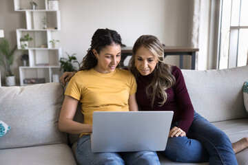 Mom and daughter look at laptop screen, discussing purchase, looking through website, search information, choosing goods or gifts, watching amusing online content, engaged in common hobby and interest