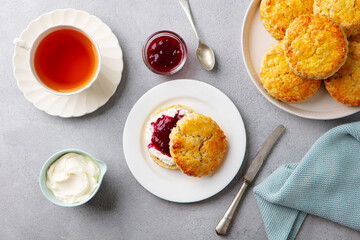 Scones, tea cakes with jam, clotted cream with tea. Traditional British teatime. Grey background. Top view.