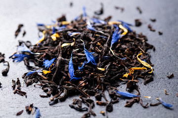 Earl grey loose leaf tea blend with cornflower and orange blossom petals on dark marble board. Close up.