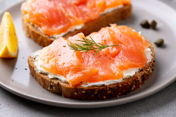 Sandwich, toast with smoked salmon and cream cheese on a plate. Grey background. Close up.
