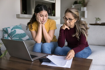 Mature Latina woman and grown-up daughter feel stressed, concerned while managing family finances,...