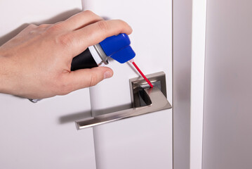 Close up of man hand using spray can to grease metal handle on white door. Home repair concept