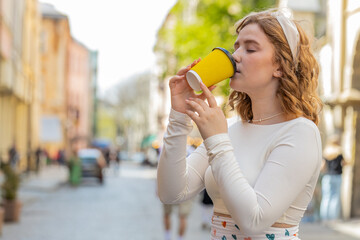 Happy redhead young woman enjoying morning coffee hot drink and smiling outdoors. Relaxing, taking...