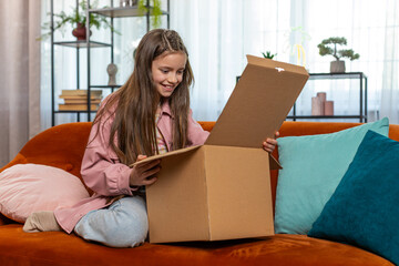 Happy amazed young child kid girl unpacking delivery parcel. Surprised satisfied teen shopper, online shop customer opening cardboard box receiving purchase gift by fast postal shipping at home.
