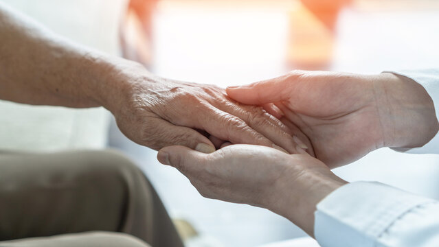 Arthritis or parkinson disease elderly patient, old aged senior woman holding geriatric doctor, cargiving nurse or family assistant's hand in hospice home for medical health care or mental therapy