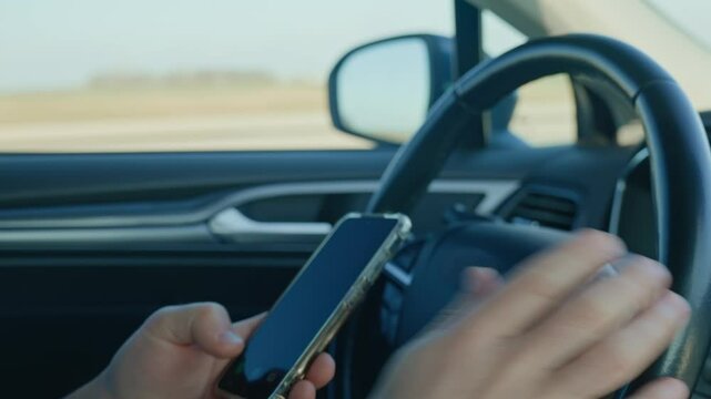 Close-up of driver hands using smartphone while driving car, risk of distraction and road safety concerns. Dangerous driving of vehicle, violation of traffic rules
