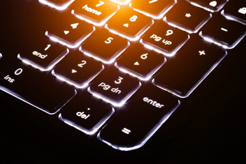 Keyboard close-up with backlight on a black background. Fragment with blurred keys.