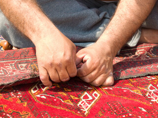 Close-up of an unrecognisable person sitting on the floor repairing a carpet, New Delhi, India