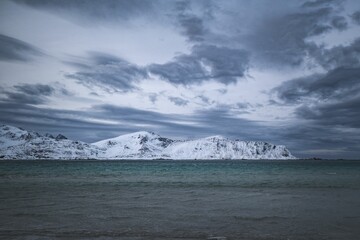 Snow-covered mountains with dramatic clouds over a serene sea in Lofoten island