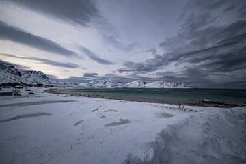 Snow-covered beach with dramatic clouds and mountains in the background
