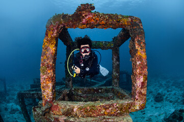 Male diver swimming through the artificial reef concrete block at Racha Yai Island, a popular dive...