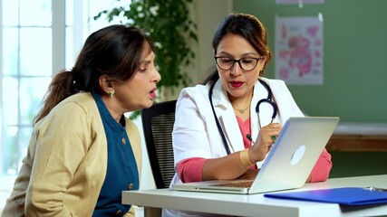Indian Asian young female doctor discussing medical case, diagnosis with senior woman patient using laptop in lavish clinic, leveraging modern technology for efficient healthcare consultation