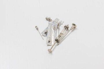 Syringe, needles and test tube on a white background. In the background a plate of medicines