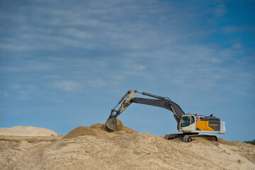 Obraz premium Heavy machinery is actively moving sand along the coastline under a clear blue sky, focusing on erosion control efforts during daylight hours in a coastal area.